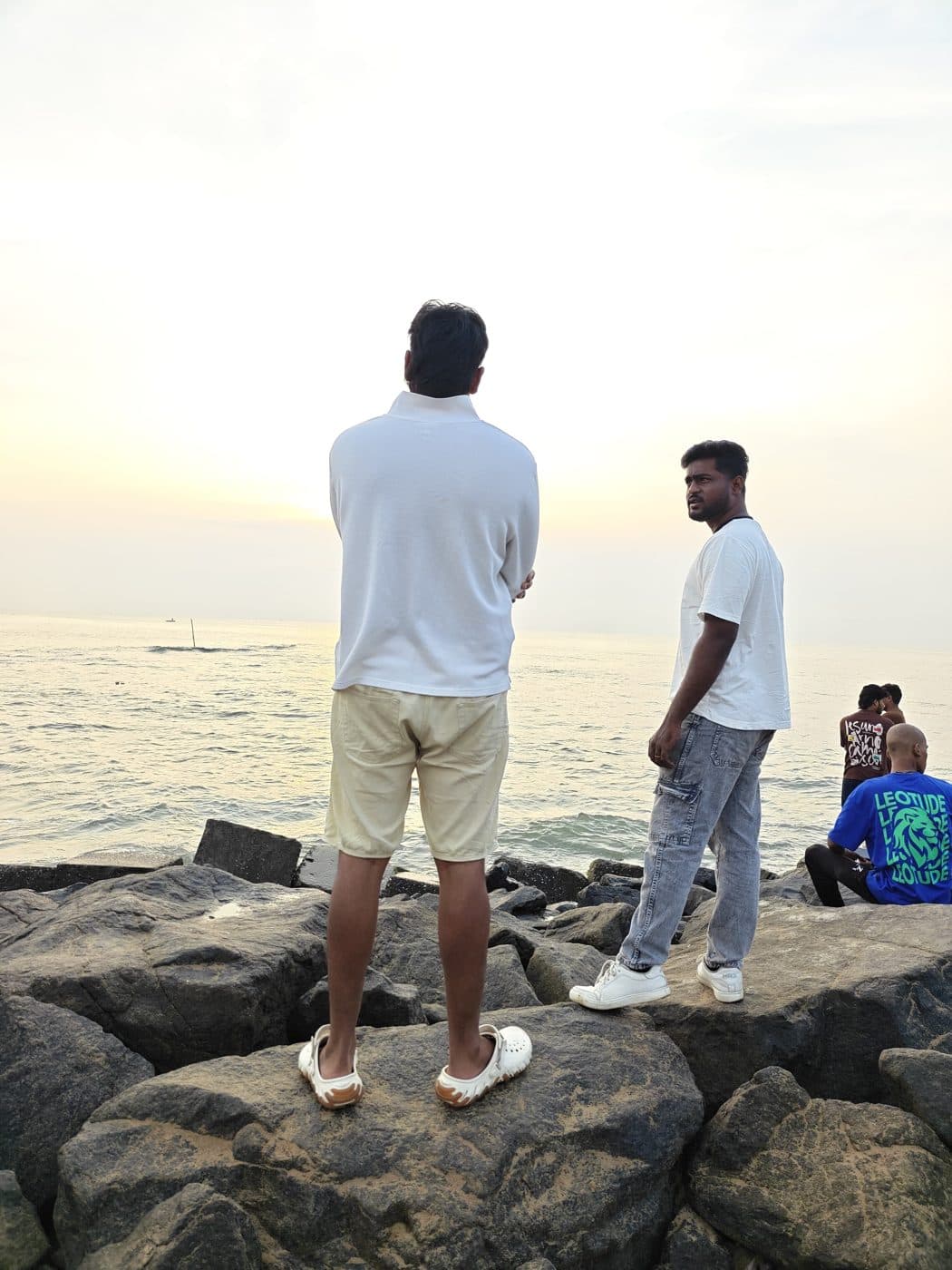 Two people standing on rocks watching the sunrise over the sea in Pondicherry.